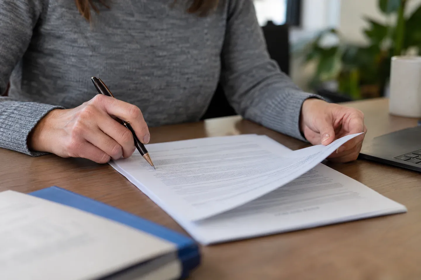 Hands carefully reviewing a document with a pen at a desk.