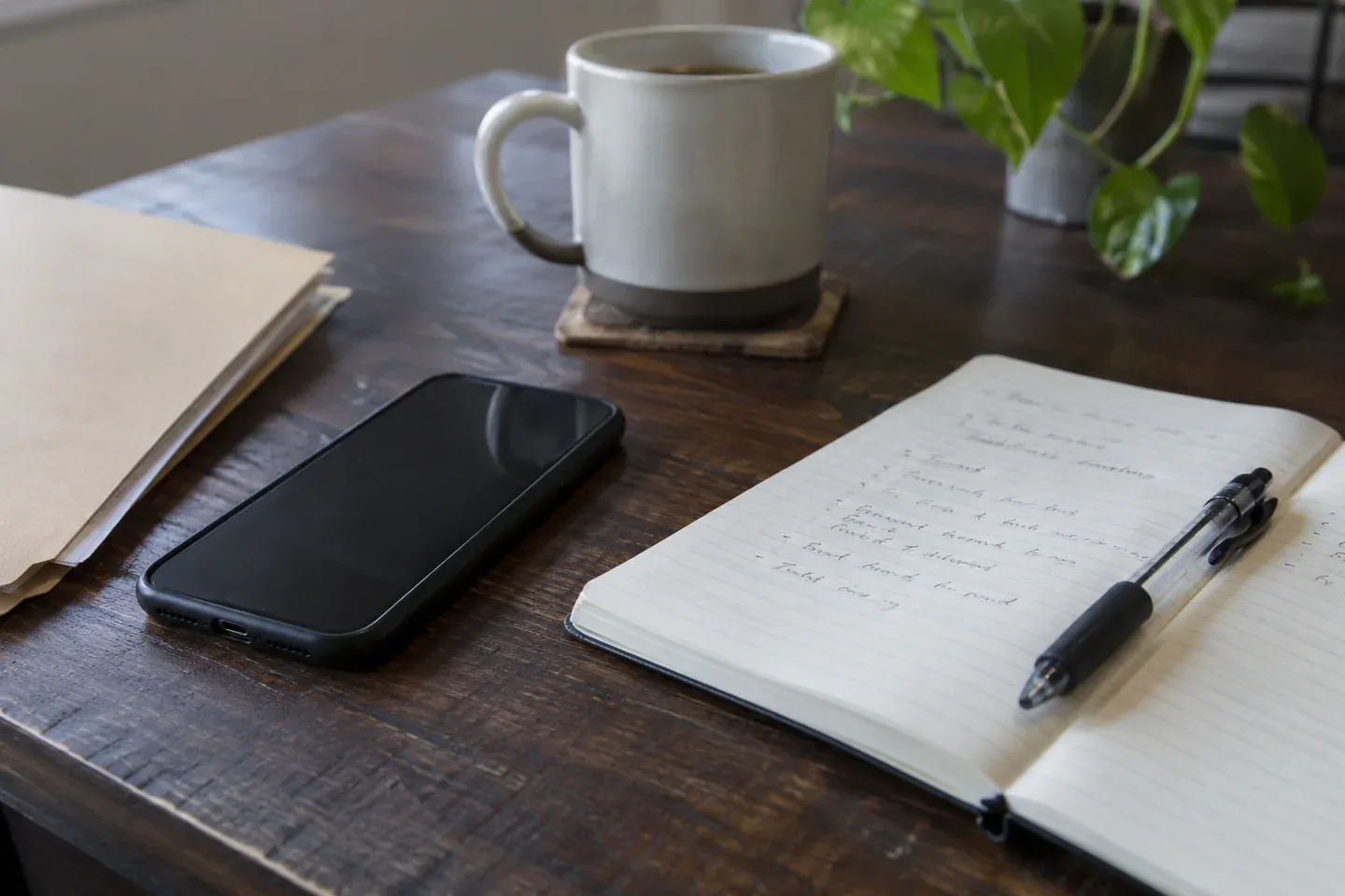 A phone, notebook, pen, mug and document folder on a desk.