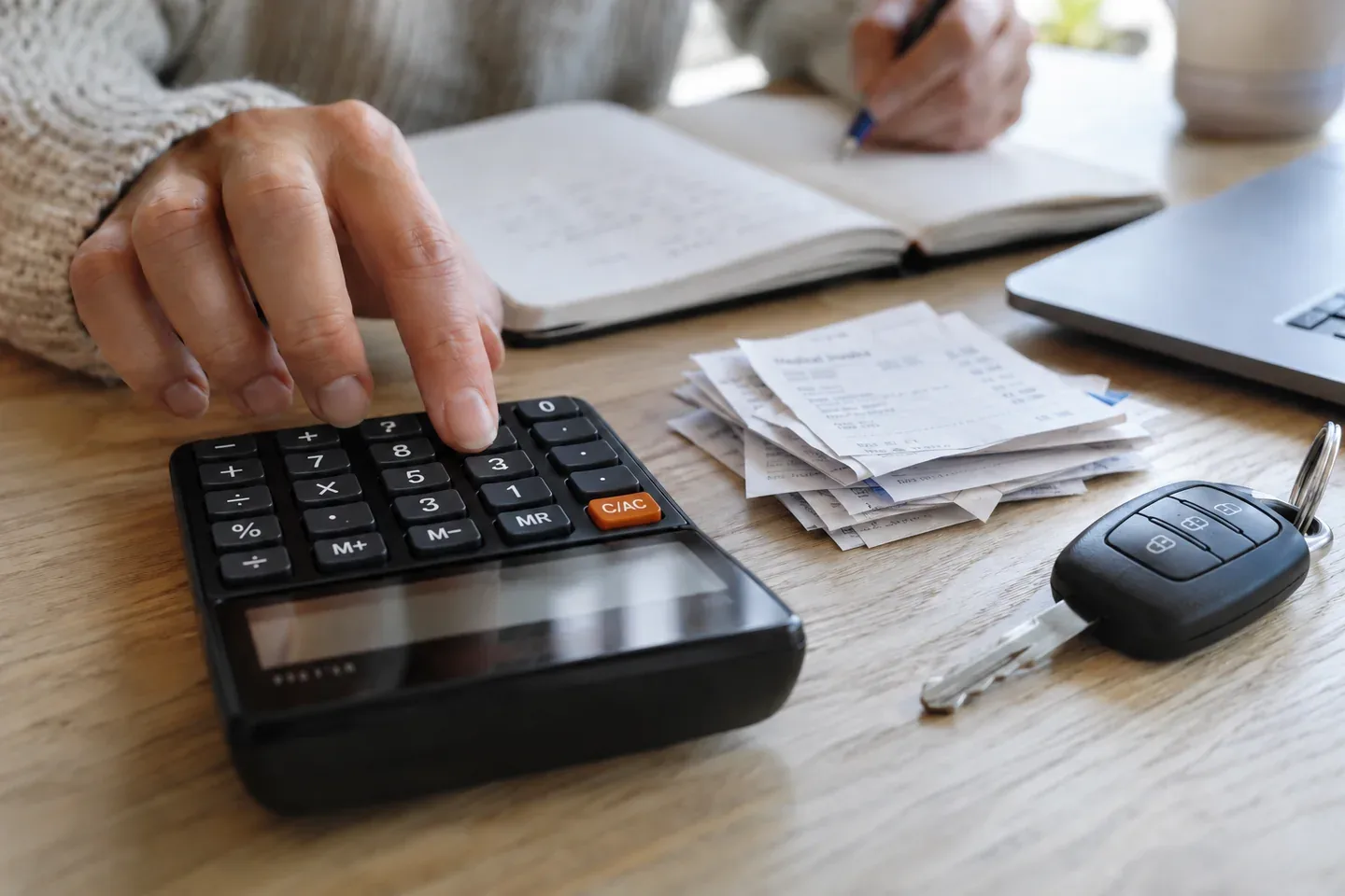 A calculator, paperwork, notebook and car key on a desk.