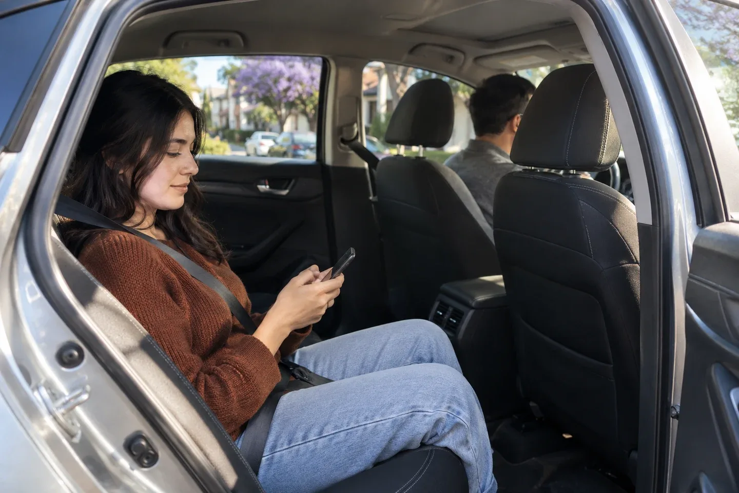 A belted passenger checks her phone in a parked sedan; AI-generated editorial illustration.